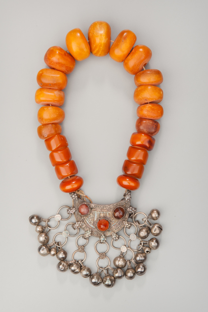 Necklace with large stone beads and an elaborate silver pendant. The silver pendant has three inlaid stones, and several round silver bells attached by connected rings.