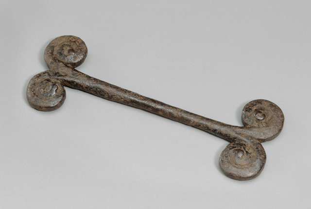 An iron form including a straight bar with two symmetrical coil shapes on either end of the bar.