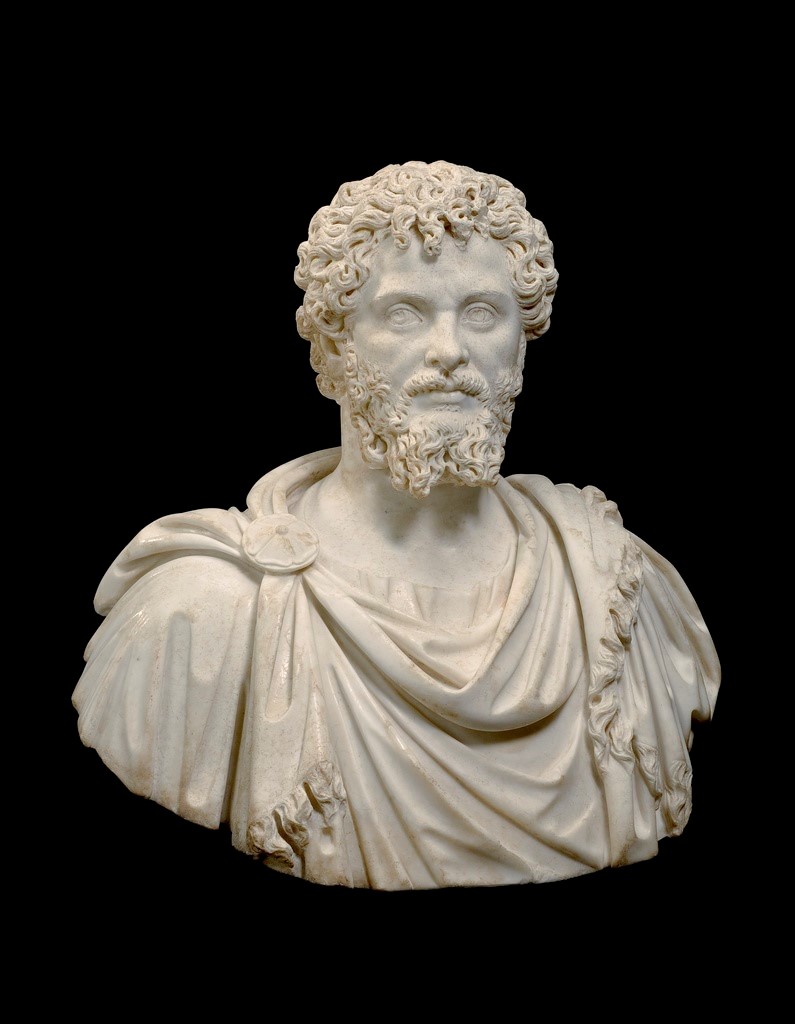 Bust of a man with curly hair and beard. He glances to his left. He wears a tunic and fringed cloak, fastened at his left shoulder with a circular brooch.