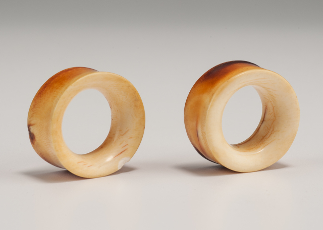 Two short ivory forms, cylindrical in shape with slightly concave edges, and each with a wide hole running through the middle. The surface of both is very smooth.