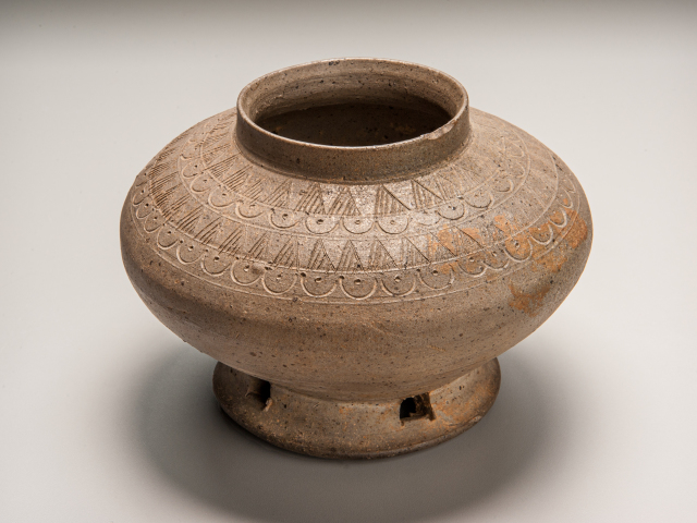 Footed bowl made of grey-brown gritty stoneware with incised decorations.